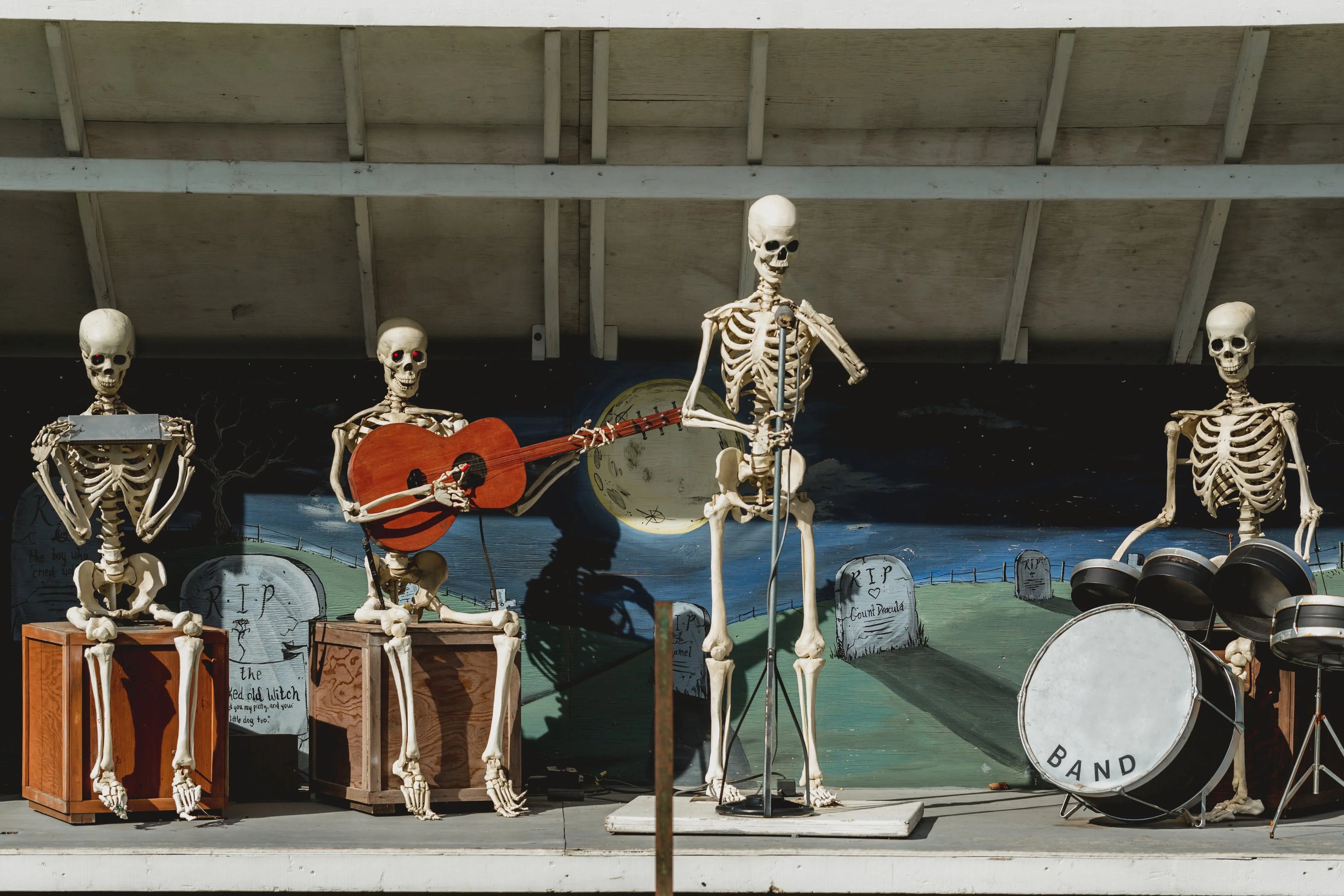 Four skeletons playing musical instruments in front of a mural.