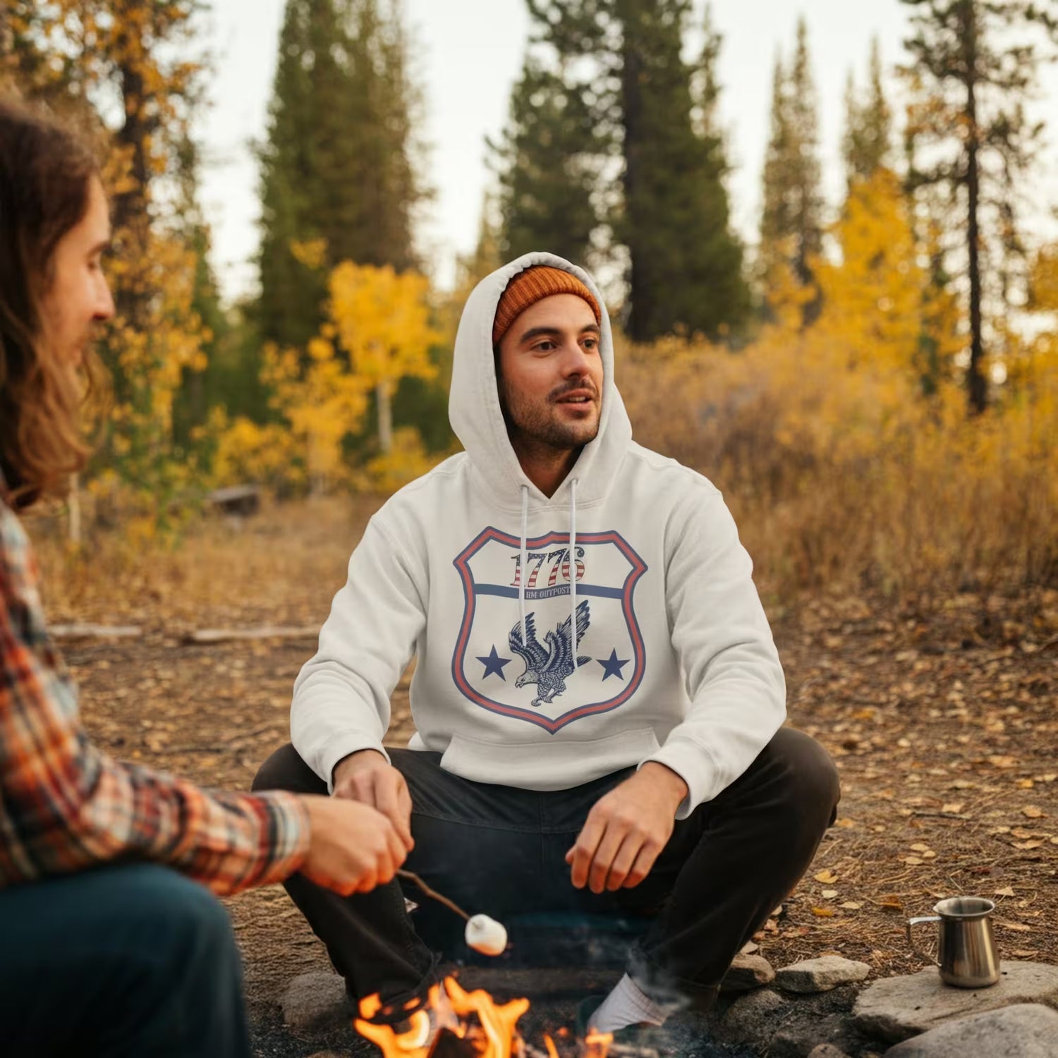 Two people sitting by a campfire in a forest with autumn foliage.